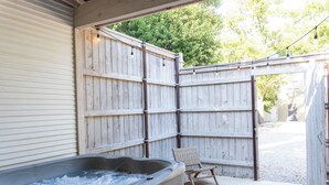 A hot tub, wooden fence, and a chair in a backyard setting. - Cozy Modern Suite in Fredericksburg (Fredericksburg)
