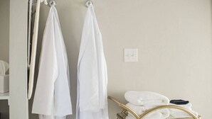 A bathroom with two white towels hanging on hooks, a gold towel rack with folded towels, and a white light switch on the wall.