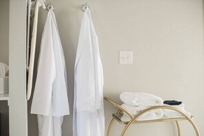 A bathroom with two white towels hanging on hooks, a gold towel rack with folded towels, and a white light switch on the wall. - Cozy Glam Suite in Fredericksburg (Fredericksburg)