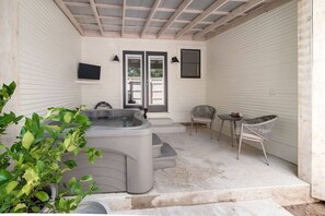 A covered patio with a hot tub, two chairs, a small table, and a TV mounted on the wall. - Cozy Glam Suite in Fredericksburg (Fredericksburg)