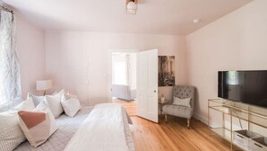 A bedroom with a bed, a TV, a chair, and a door leading to another room.