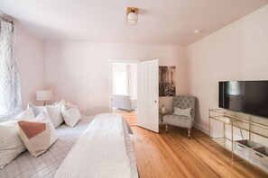 A bedroom with a bed, a TV, a chair, and a door leading to another room. - Cozy Glam Suite in Fredericksburg (Fredericksburg)