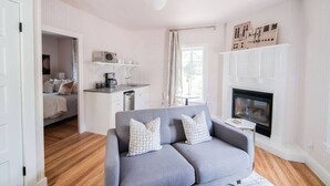 A modern living room with a grey sofa, a fireplace, and a kitchen area visible through an open door.