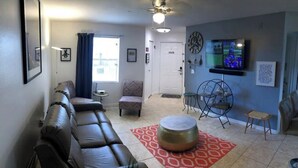 A living room with a sofa, ottoman, and a TV mounted on the wall. - Next Door To It All! Disney/Dining & More mins away 2Bed 2Bth Condo (Kissimmee)