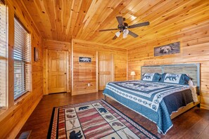 A wooden cabin bedroom with a bed, a ceiling fan, and a rug with animal prints. - Luxe Pool Cabin w/MTN views! Hot Tub + Theater (Pigeon Forge)