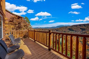 A wooden deck with a railing, two wicker chairs, and a view of a mountainous landscape. - Luxe Pool Cabin w/MTN views! Hot Tub + Theater (Pigeon Forge)