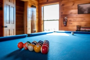 Een biljart met ballen in een houten kamer met een deur en een raam.