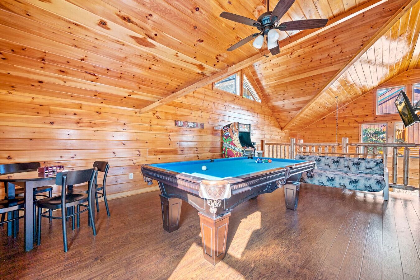 A wooden cabin with a pool table, chairs, and a ceiling fan.