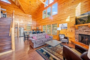 A cozy cabin interior with a wooden interior, a fireplace, a sofa, and a dining area. - Luxe Pool Cabin w/MTN views! Hot Tub + Theater (Pigeon Forge)