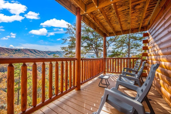 Une terrasse en bois avec une rambarde, un espace abrité et une vue sur un paysage montagneux.