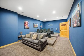A home theater room with blue walls, a gray sofa, and multiple rows of seating. - Luxe Pool Cabin w/MTN views! Hot Tub + Theater (Pigeon Forge)