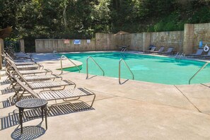 A swimming pool with lounge chairs and a table, surrounded by a concrete deck and a wooden fence. - Luxe Pool Cabin w/MTN views! Hot Tub + Theater (Pigeon Forge)