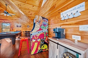 L’intérieur d’un chalet en bois chaleureux et accueillant, avec une table de billard, un tabouret rouge, un coin café et une fresque murale colorée.
