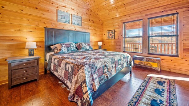 Een houten slaapkamer met een bed, twee nachtkastjes, een plafondventilator en een groot raam met jaloezieën.