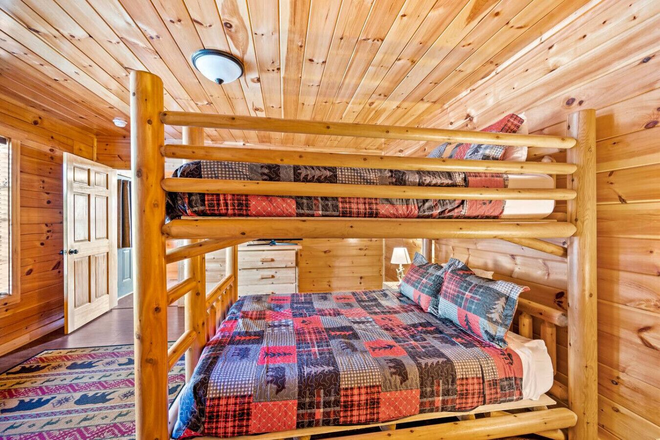 A bunk bed with a quilted bedspread and pillows, wooden walls, and a ceiling light.