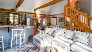 A log cabin interior with a kitchen, dining area, and a cozy living room with a sofa and chairs. - Cozy Cabin Inn w/ Private Hot Tub, Fire Pit + close to Golf, Trails, Waterfalls (Owen Sound)