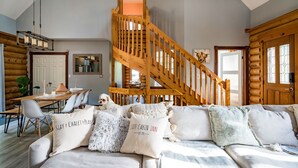 A cozy cabin interior with a wooden staircase, a dining area, and a sofa with decorative pillows. - Cozy Cabin Inn w/ Private Hot Tub, Fire Pit + close to Golf, Trails, Waterfalls (Owen Sound)