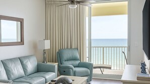 Ein modernes Wohnzimmer mit einer Couch, Sesseln, einem Couchtisch und einem Fernseher. Ein Balkon bietet Blick auf den Ozean.
