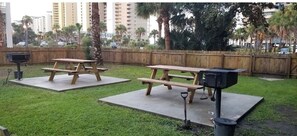 Two picnic tables with barbecue grills in a grassy outdoor area.