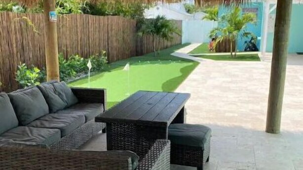 An outdoor patio area with a thatched roof, wicker furniture, and a small artificial green lawn. - Lovely 1 Bedroom with a Pool (Jupiter)