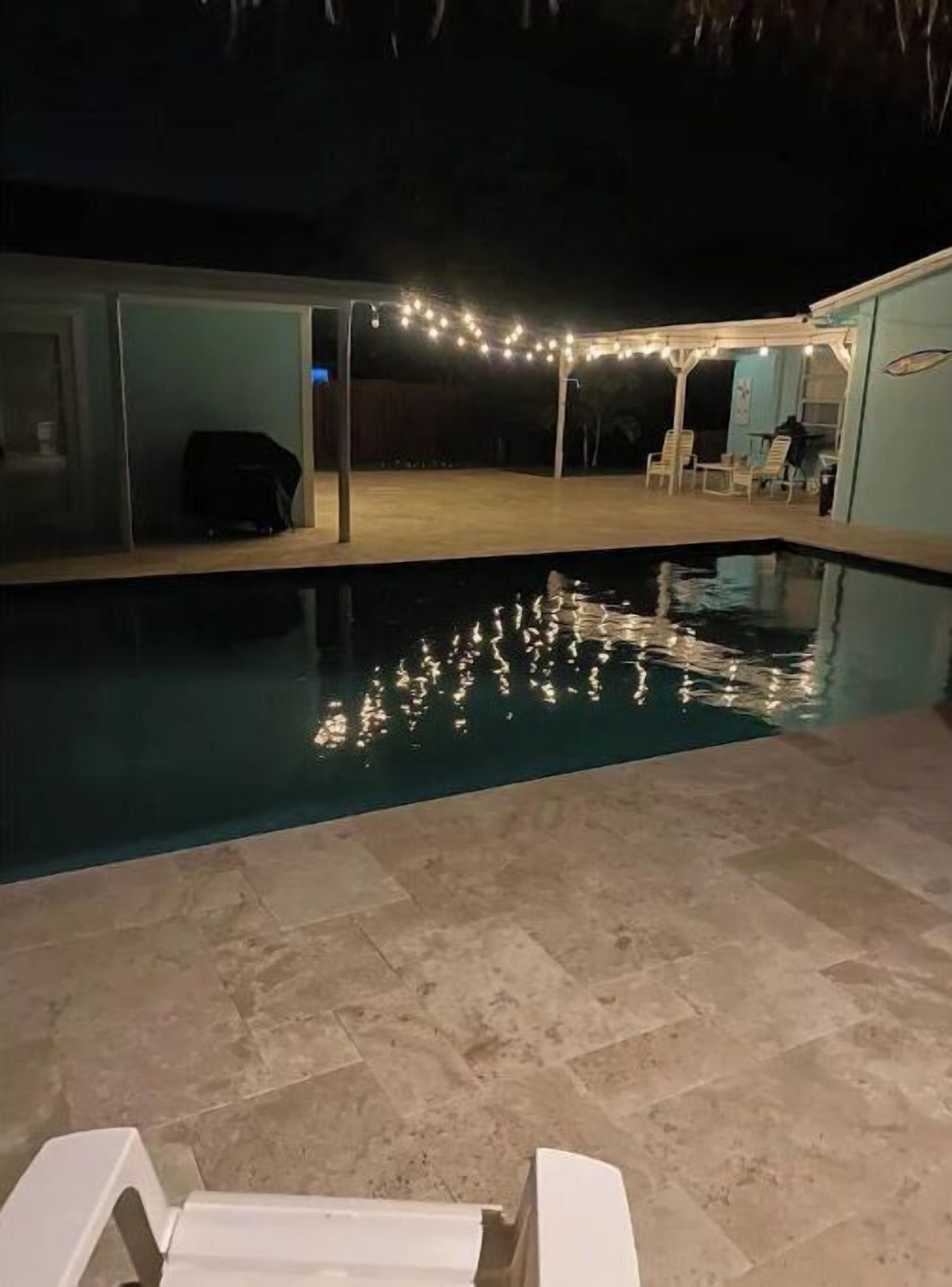 A swimming pool with tiled flooring and a few lounge chairs.