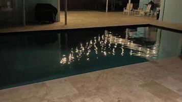 A swimming pool with tiled flooring and a few lounge chairs.