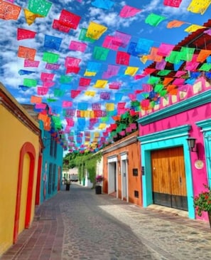 A street with colorful buildings and a sky filled with hanging decorations. - Los Nardos Hostel  (Oaxaca)