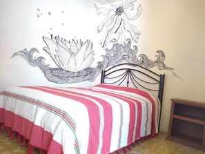 A bed with a striped bedspread, a decorative wall mural, and a metal headboard. - Los Nardos Hostel  (Oaxaca)