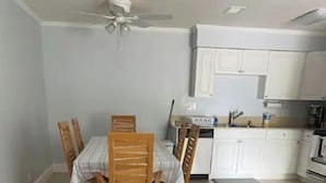 A dining area with a wooden table and chairs, a kitchen in the background, and a ceiling fan. - Lovely 2 Bedroom with a Pool (Jupiter)