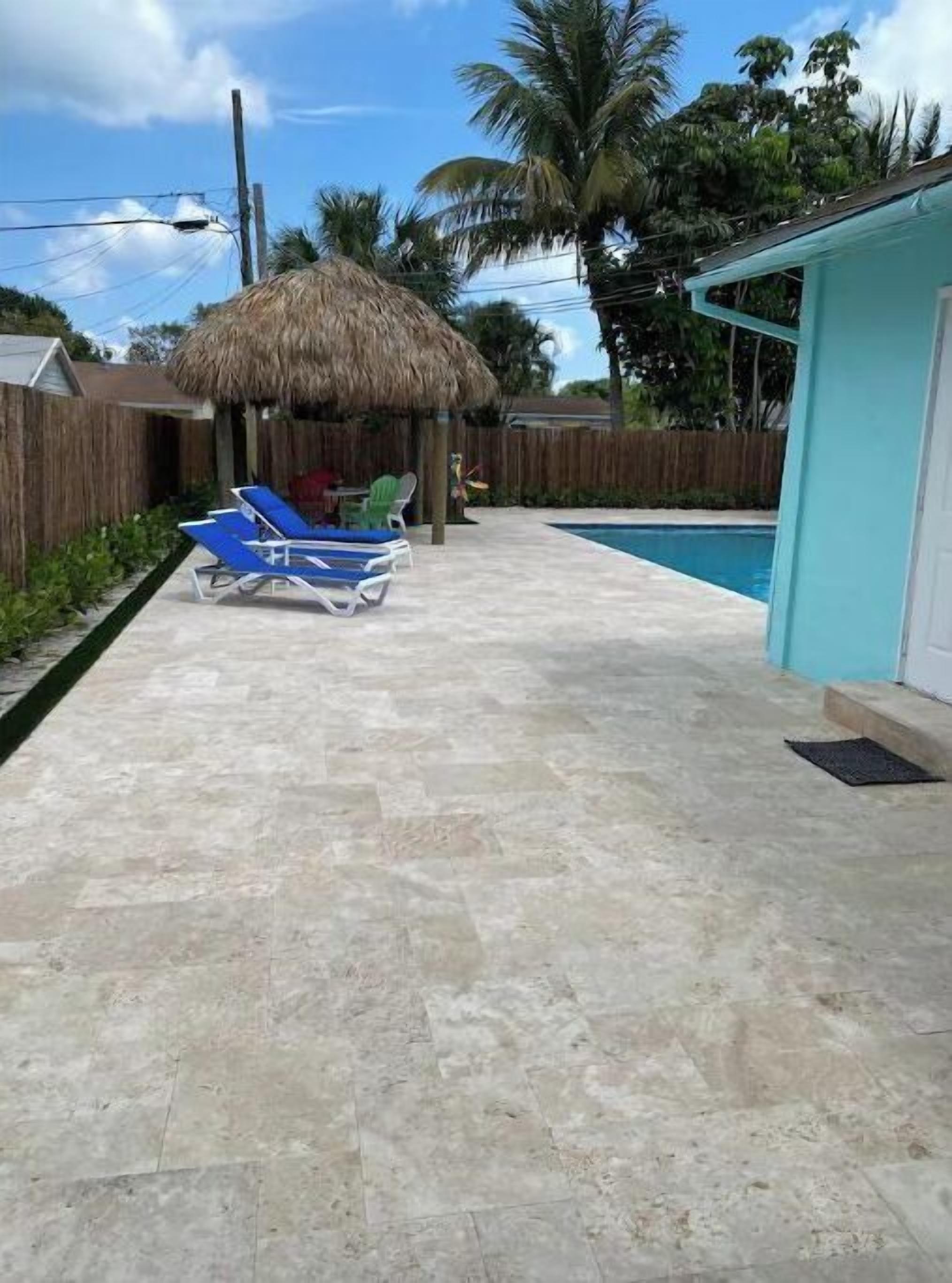 Un patio trasero con piscina, una estructura de techo de paja y un sillón de descanso azul.