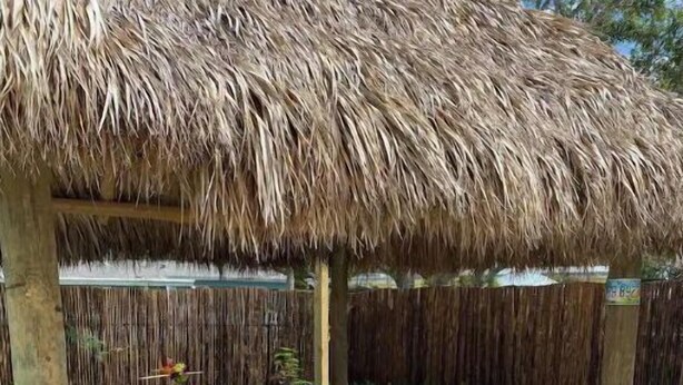 A covered outdoor seating area with a thatched roof, cushioned seating, and a stone floor. - Lovely 2 Bedroom with a Pool (Jupiter)