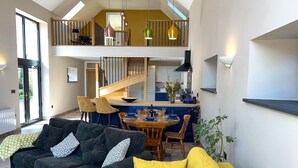 A spacious living area with a high ceiling, a dining table set for four, and a kitchen in the background. - Gloriously rural, Y Felin is a fantastic luxury barn conversion in Pembrokeshire (Ambleston)