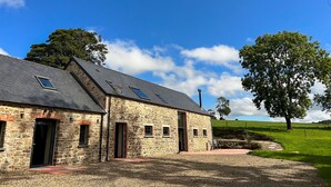 A stone building with a sloped roof and multiple windows, surrounded by a gravel driveway and a grassy field. - Gloriously rural, Y Felin is a fantastic luxury barn conversion in Pembrokeshire (Ambleston)