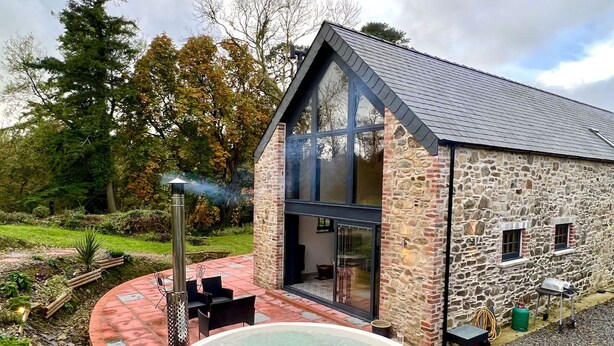A stone building with a large glass window, a hot tub, and outdoor seating. - Gloriously rural, Y Felin is a fantastic luxury barn conversion in Pembrokeshire (Ambleston)