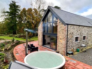 A stone building with a large glass window, a hot tub, and outdoor seating. - Gloriously rural, Y Felin is a fantastic luxury barn conversion in Pembrokeshire (Ambleston)