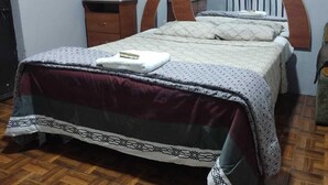 A bedroom with a wooden floor, a bed with a patterned bedspread, a wooden nightstand, and a dresser.