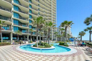 Un hôtel avec une piscine, des palmiers et un ciel bleu azur.