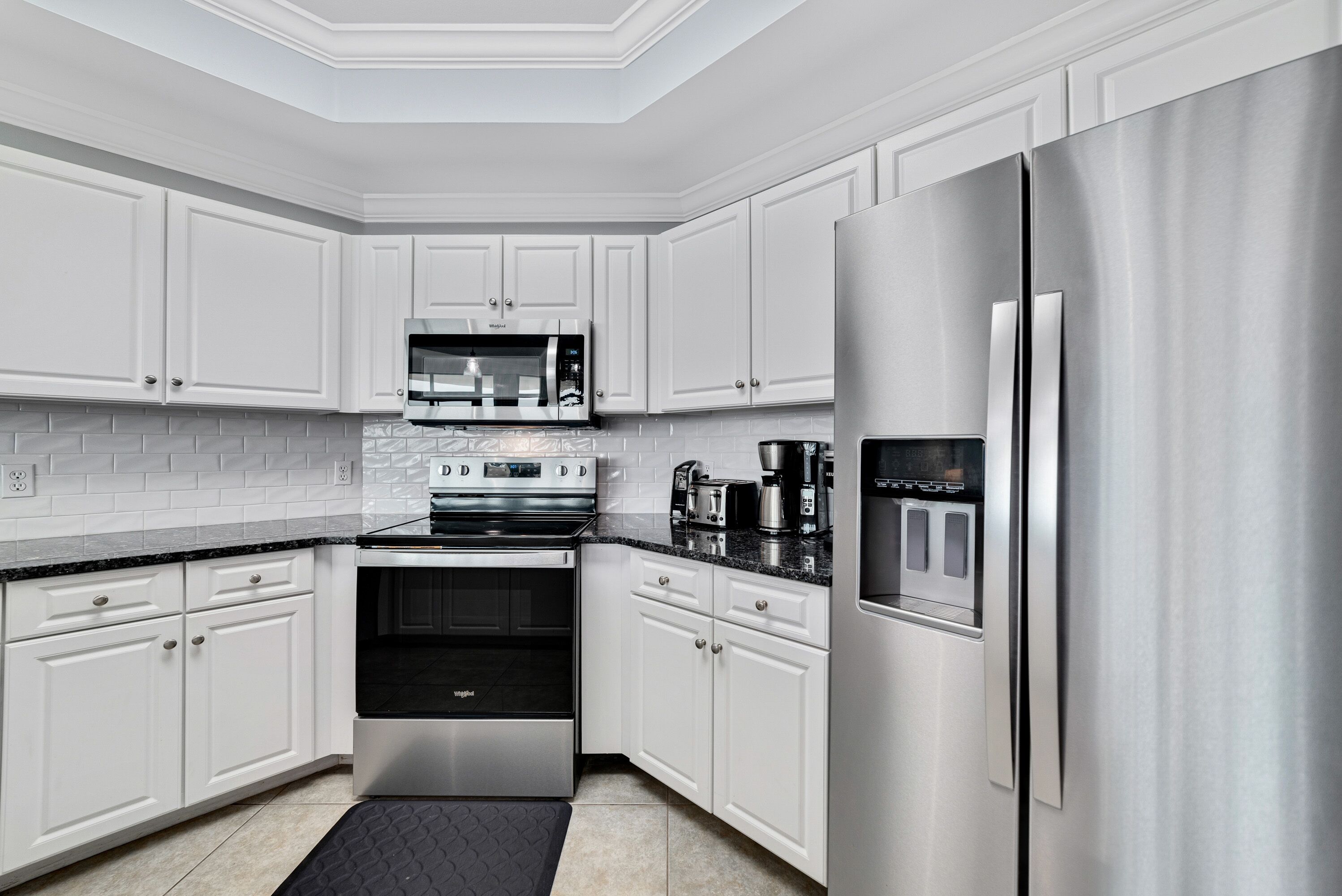 A modern kitchen with white cabinets, stainless steel appliances, and a black countertop.