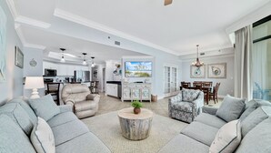 A spacious living room with a large sectional sofa, a round coffee table, and a television in the background. - Phoenix West 2207 Upscale Luxury | Updated | Beachfront | Waterslide-Lazy River (Orange Beach)