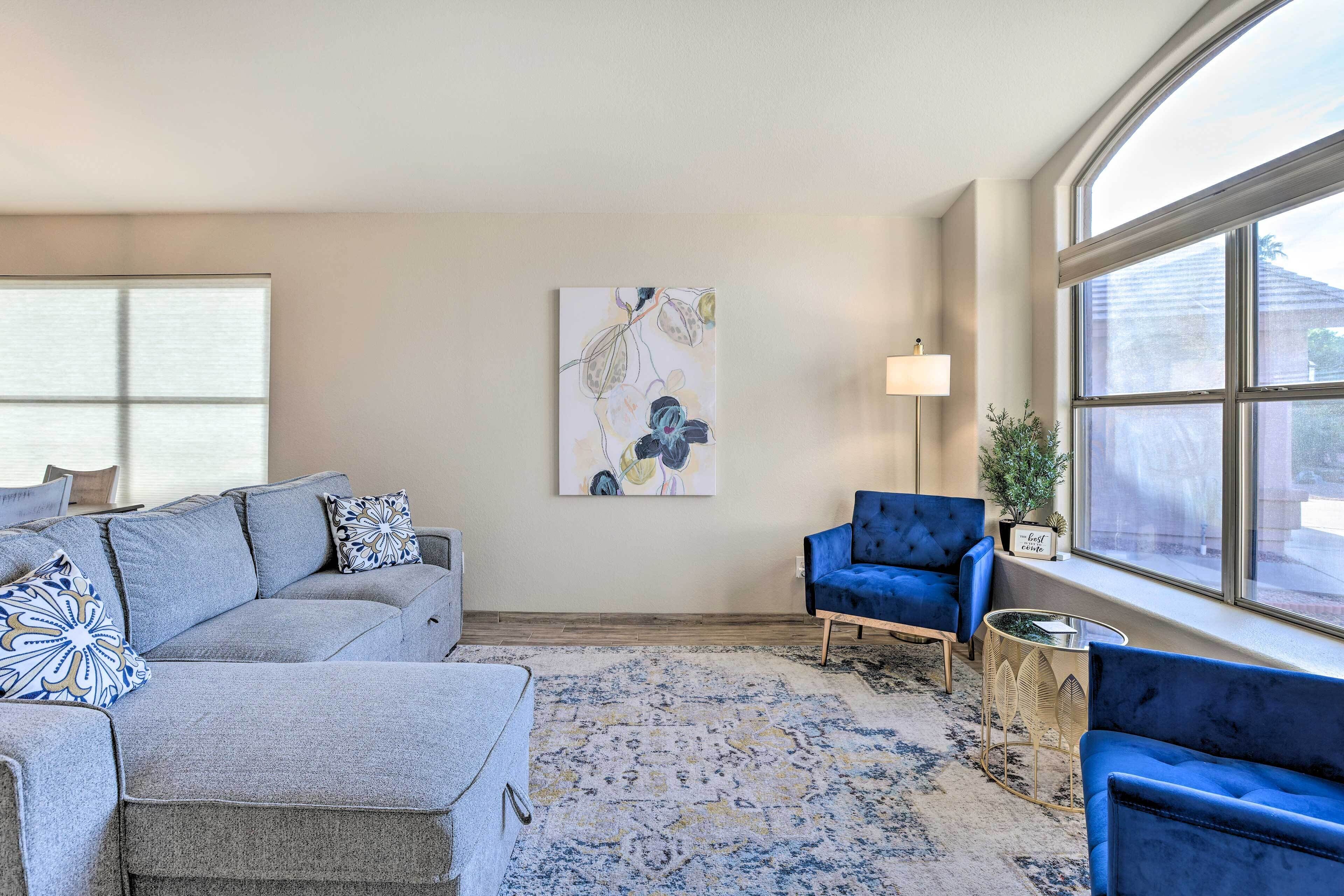 Una sala de estar con un sofá modular gris, un sillón azul y una alfombra estampada.