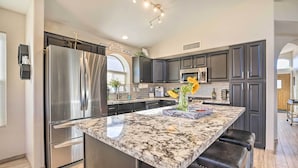 A modern kitchen with dark cabinets, stainless steel appliances, and a marble island with stools. - Close to Spring Training! Serene Retreat in Gibert (Gilbert)