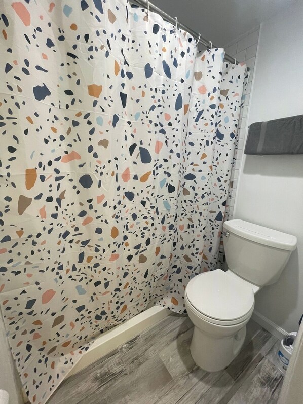 A bathroom with a shower curtain featuring a terrazzo pattern, a white toilet, and a wooden floor.