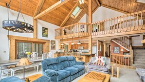 Un'ampia zona giorno con soffitto alto, travi in legno, un tavolo da pranzo, divani blu e una scala che conduce a un livello superiore.