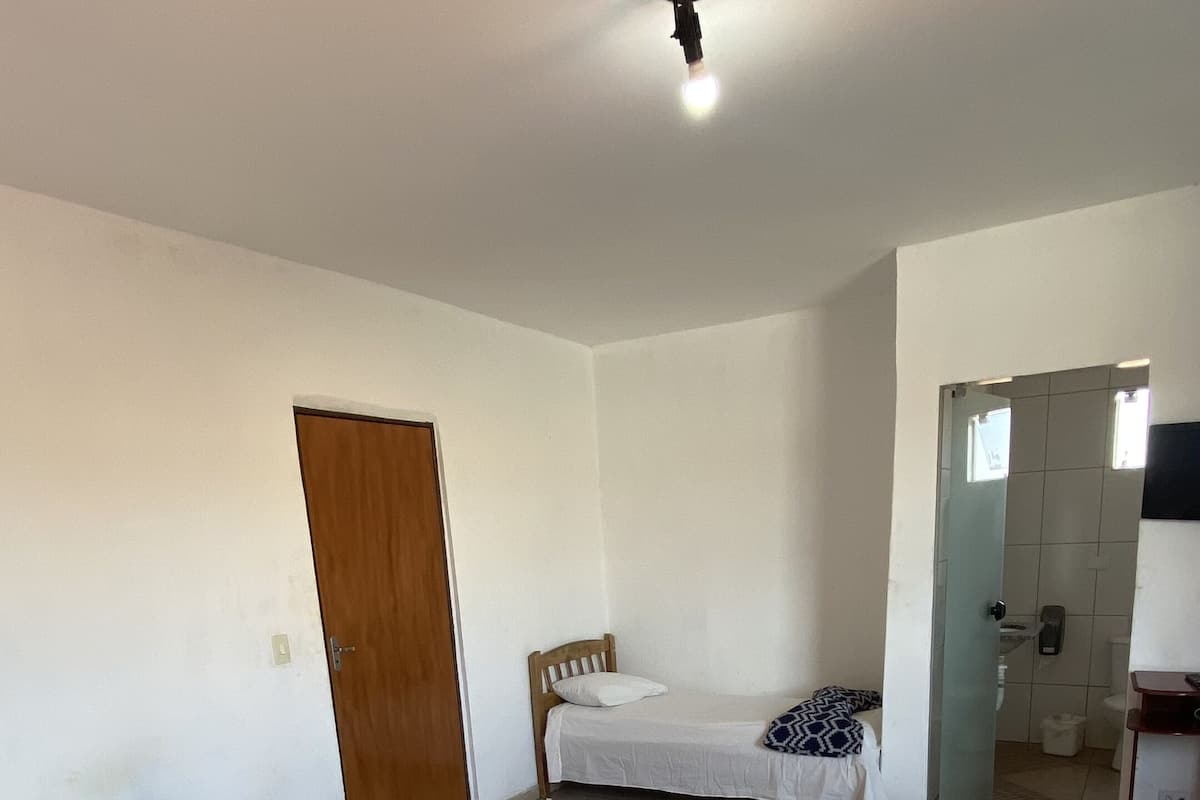 A room with two beds, a wooden door, a bathroom visible through an open door, and a ceiling light.