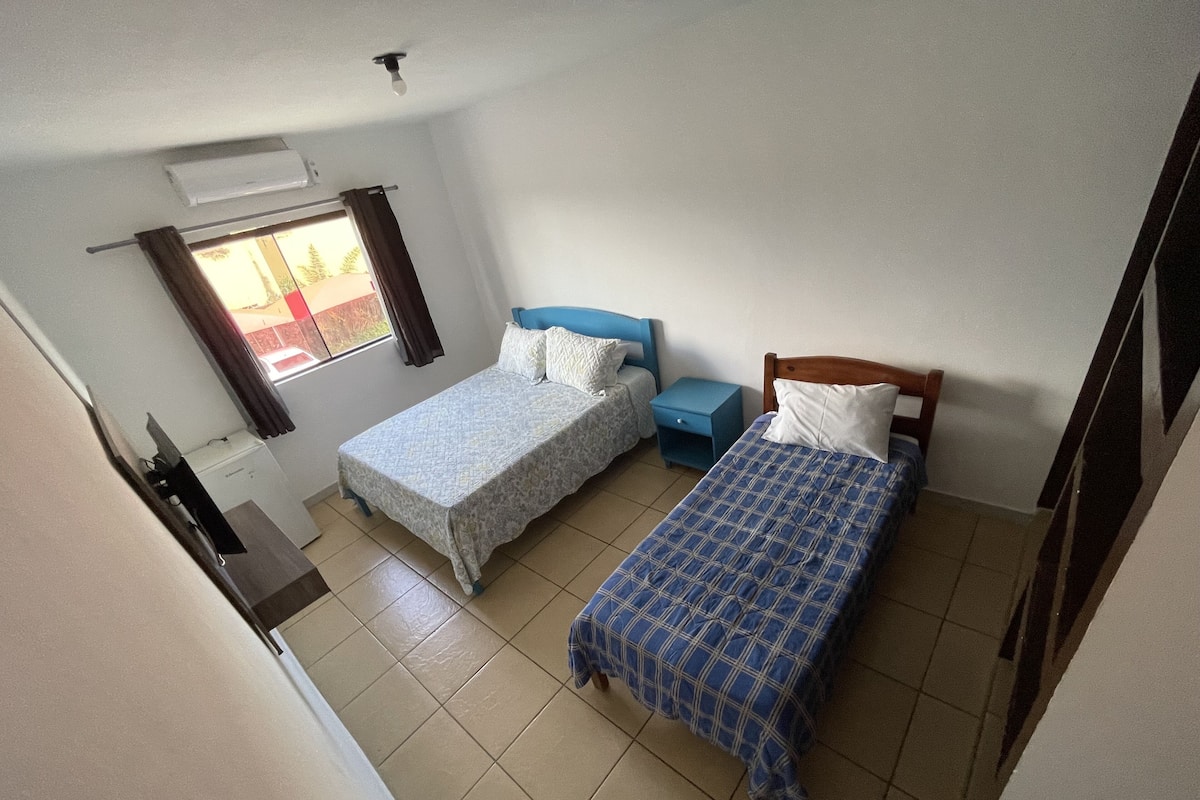 A small, clean room with two beds, a window, and a ceiling fan.