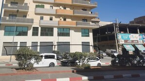 Un immeuble résidentiel à plusieurs étages, doté de balcons, d’un espace de stationnement et surplombant un ciel bleu dégagé.