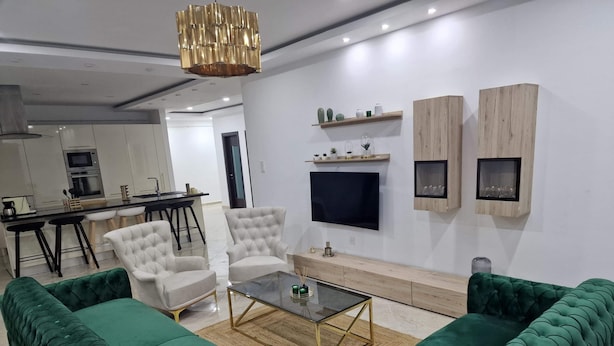 Un salon moderne avec un canapé vert, une table basse en verre et un téléviseur fixé au mur.