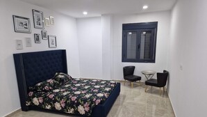 Une chambre à coucher avec un lit, deux chaises, une petite table et une fenêtre avec des stores.