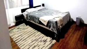 Une chambre à coucher avec un lit, une fenêtre avec des rideaux, un tableau au mur et un tapis sur le sol.