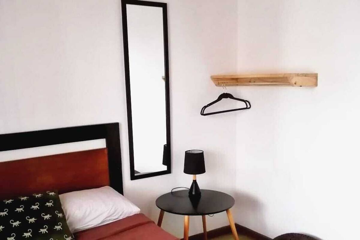 A bedroom with a bed, a bedside table, a hanging light, a mirror, and a small round rug.